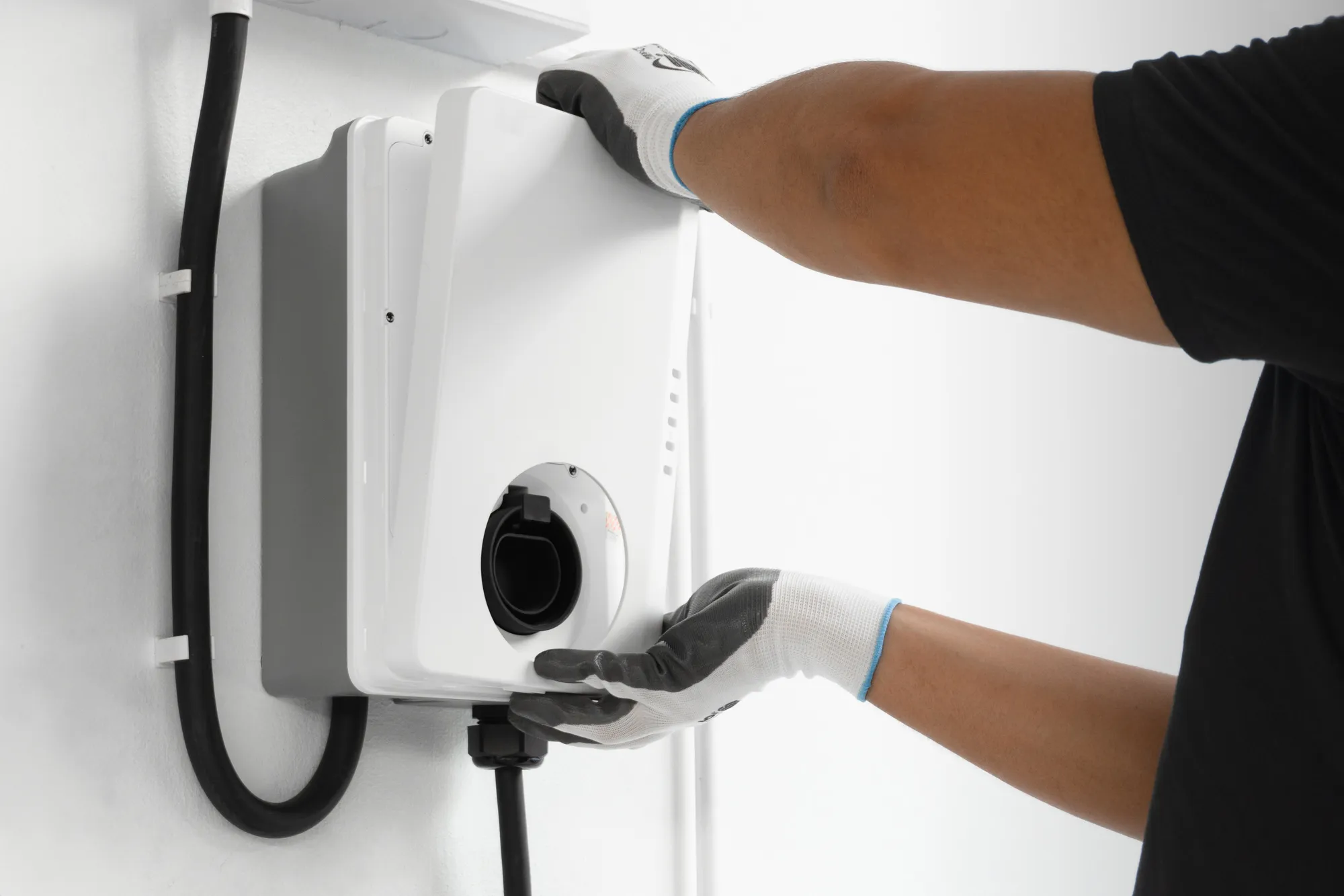 Technician in work gloves mounting a wall-mounted EV charger