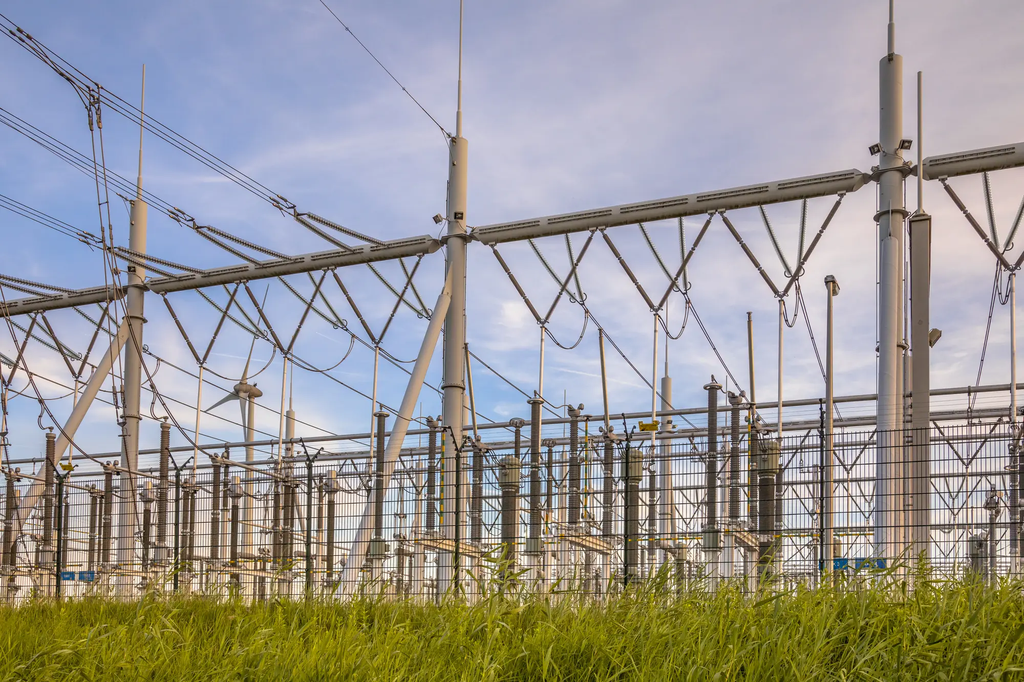 Utility substation gantries and high-voltage lines above a grassy field